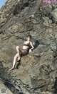 A woman in a bikini sitting on a rock.