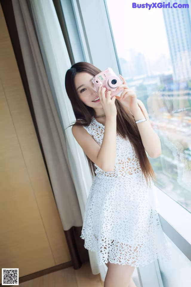 A woman in a white dress holding a pink camera.