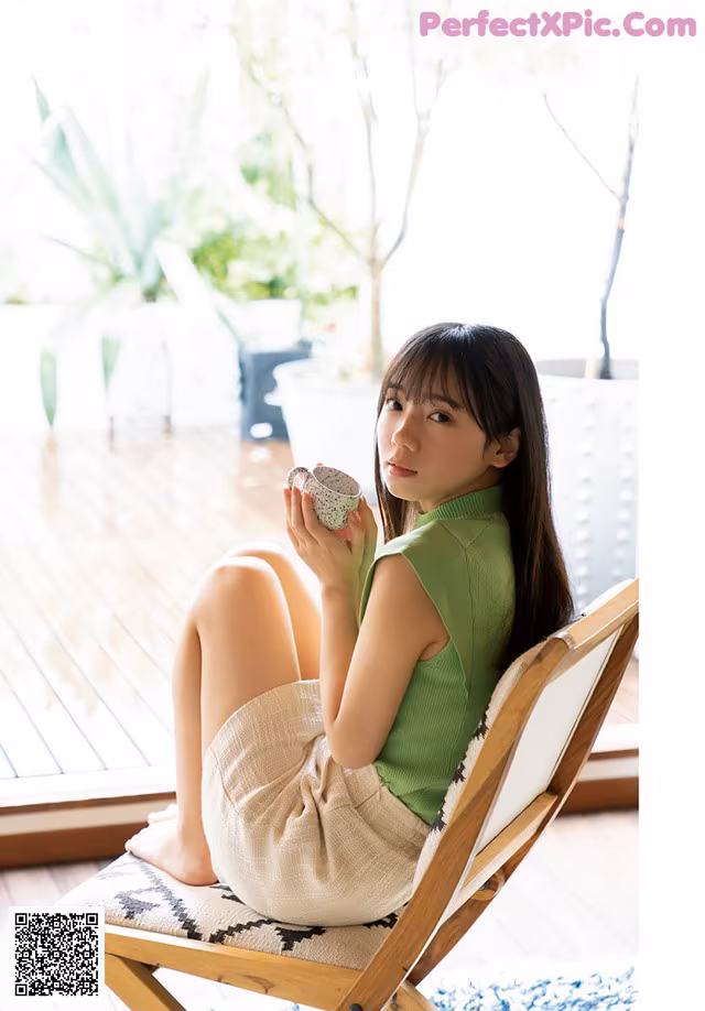 A woman sitting in a chair holding a cup of coffee.