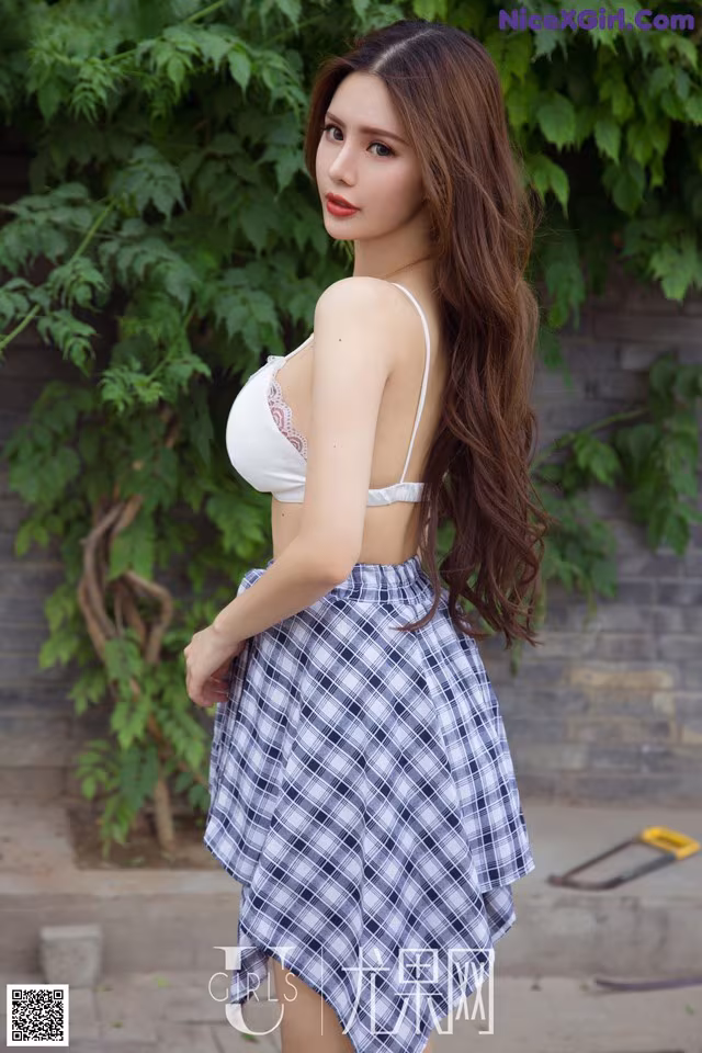 A woman in a white top and blue plaid skirt posing for a picture.