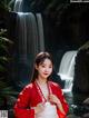 A woman in a red and white dress standing in front of a waterfall.