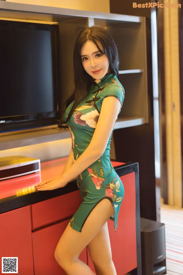 A woman in a green dress posing in front of a television.