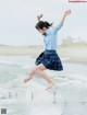 A woman in a school uniform jumping in the air on the beach.