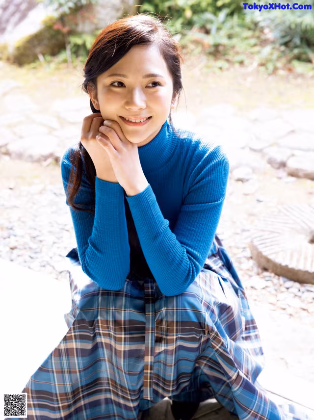 A woman in a blue sweater and plaid skirt posing for a picture.