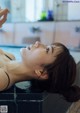 A woman in a black bikini laying in a bathtub.