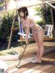 A woman in a bikini cleaning a deck with a mop.