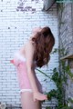 A woman in a pink lingerie leaning against a brick wall.