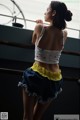 A woman in a white top and blue skirt leaning against a railing.