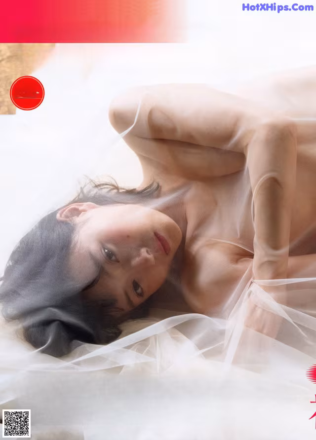 A woman laying on top of a bed covered in a white sheet.