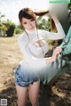 A woman in a white top and denim shorts posing in front of a tractor.